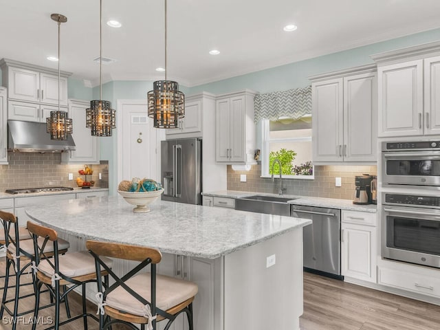 kitchen featuring under cabinet range hood, a kitchen island, a sink, appliances with stainless steel finishes, and backsplash