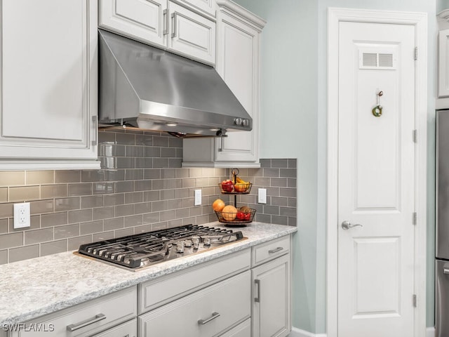 8524 Sevilla Ct, Naples, FL 34114 - kitchen with under cabinet range hood, stainless steel gas stovetop, backsplash, and white cabinetry