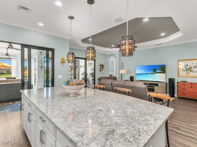 8524 Sevilla Ct, Naples, FL 34114 - kitchen featuring a chandelier, a tray ceiling, ornamental molding, wood finished floors, and light stone countertops