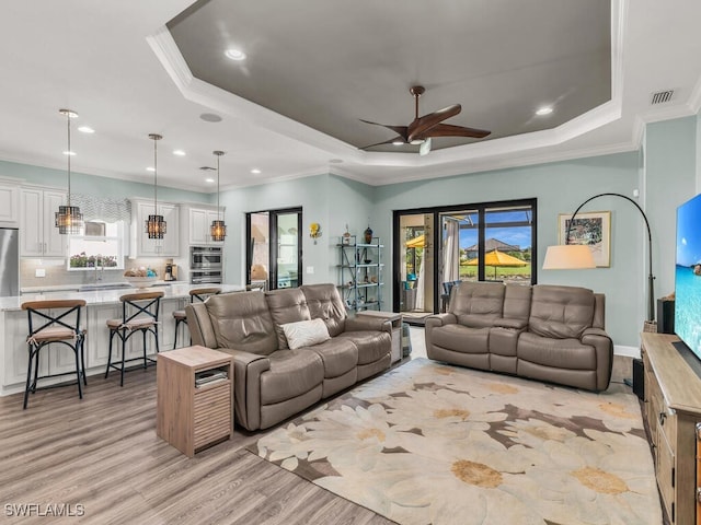 living area with light wood-type flooring, a wealth of natural light, a raised ceiling, and crown molding