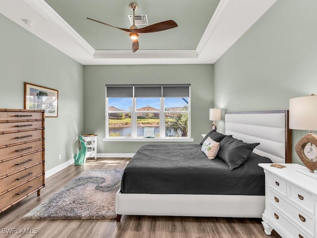 bedroom featuring crown molding, a raised ceiling, visible vents, wood finished floors, and baseboards