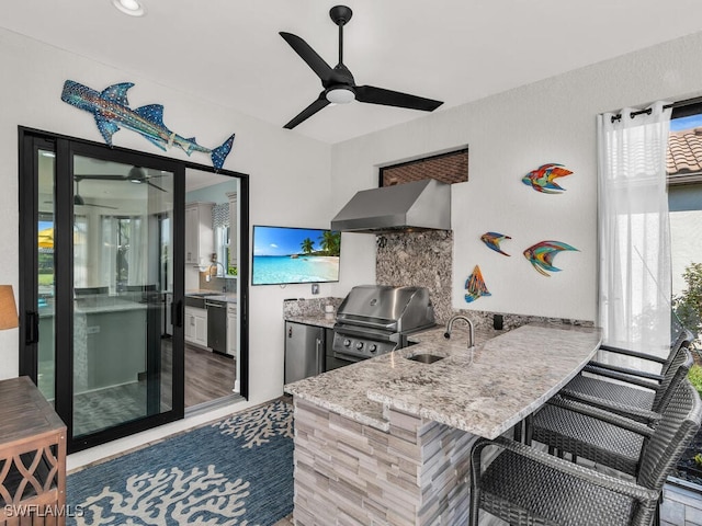 kitchen with dishwashing machine, a sink, a ceiling fan, light stone countertops, and wall chimney exhaust hood