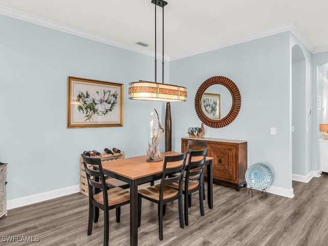 dining room featuring arched walkways, wood finished floors, visible vents, baseboards, and crown molding