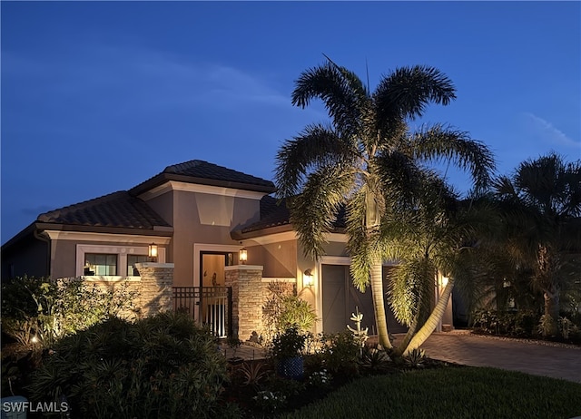 view of front of home with decorative driveway, stucco siding, an attached garage, fence, and stone siding