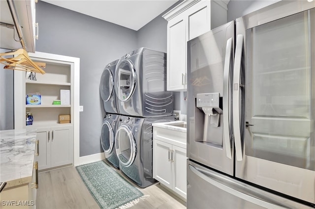 clothes washing area featuring cabinets, stacked washer / dryer, and light wood-type flooring