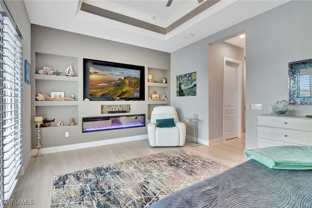 interior space with a tray ceiling, built in shelves, and light hardwood / wood-style flooring