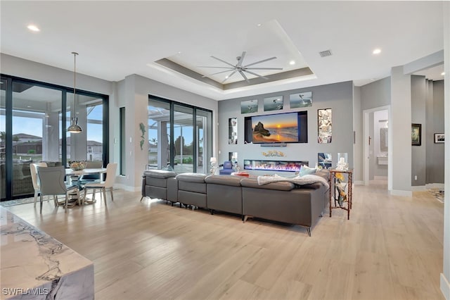 living room featuring ceiling fan, light wood-type flooring, and a tray ceiling