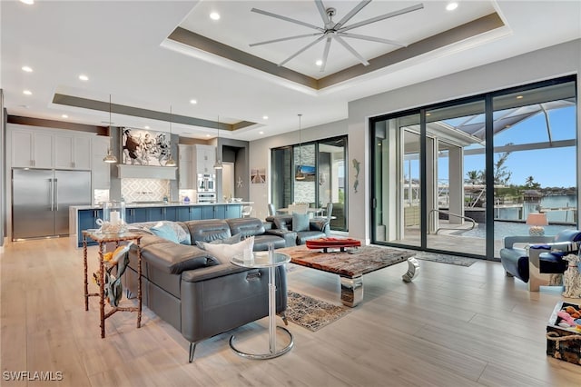 living room featuring ceiling fan, a tray ceiling, and light hardwood / wood-style floors