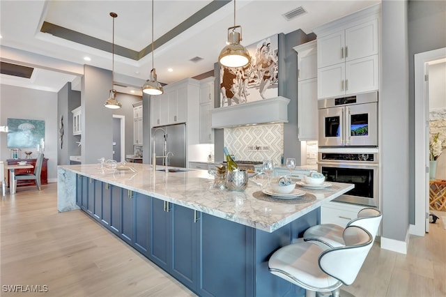 kitchen featuring pendant lighting, stainless steel appliances, a raised ceiling, and a large island with sink