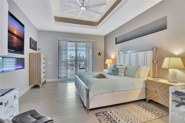 bedroom with a raised ceiling, access to outside, ceiling fan, and light hardwood / wood-style flooring