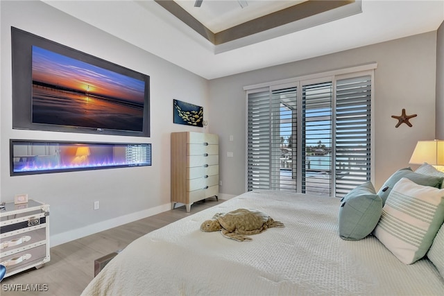 bedroom with access to exterior, a raised ceiling, and light hardwood / wood-style flooring