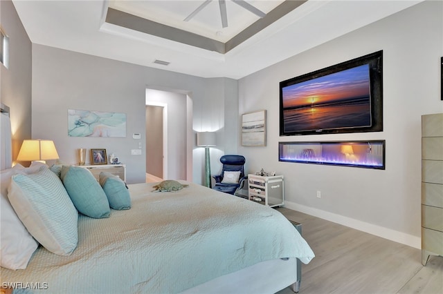 bedroom featuring a tray ceiling, ceiling fan, and light wood-type flooring