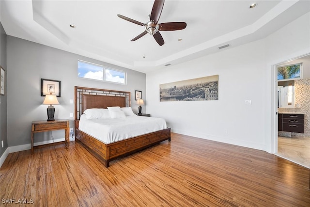 bedroom with a tray ceiling, connected bathroom, ceiling fan, and light hardwood / wood-style flooring