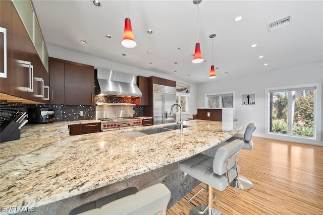 kitchen with dark brown cabinetry, wall chimney exhaust hood, decorative light fixtures, a breakfast bar, and high end appliances