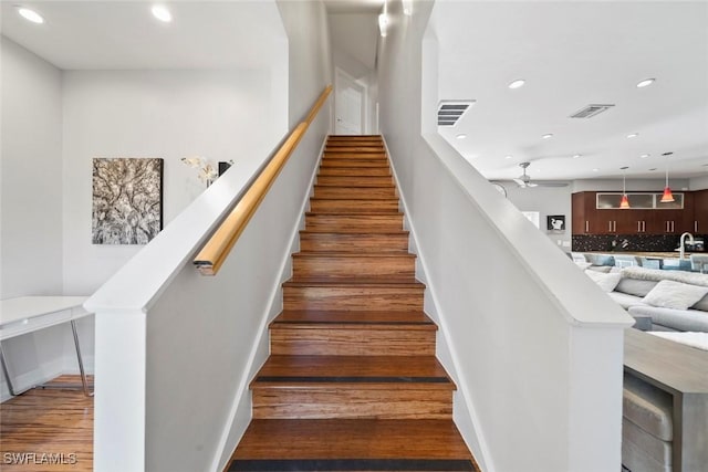 staircase with ceiling fan, wood-type flooring, and sink