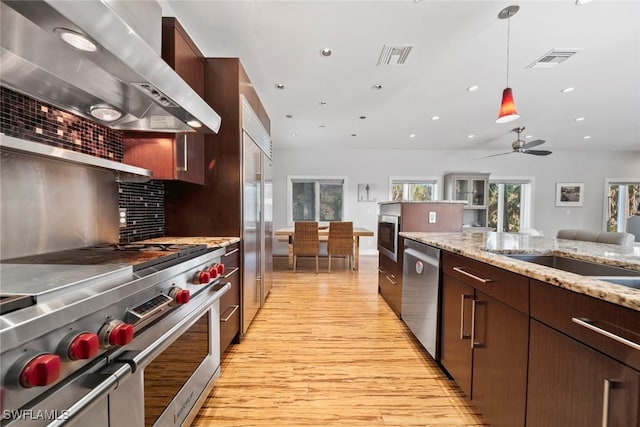 kitchen featuring decorative backsplash, stainless steel appliances, ceiling fan, wall chimney range hood, and light hardwood / wood-style flooring