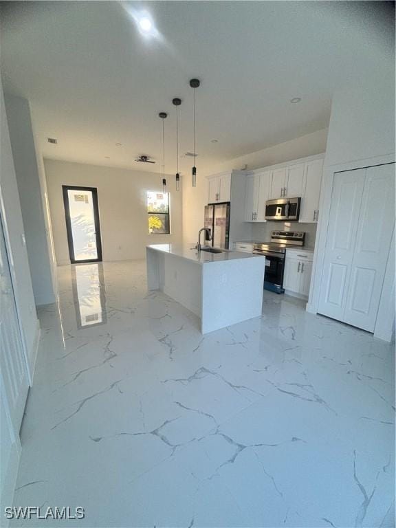 1115 Cumming St E, Lehigh Acres, FL 33974 - kitchen with stainless steel appliances, white cabinetry, decorative light fixtures, a center island with sink, and light countertops
