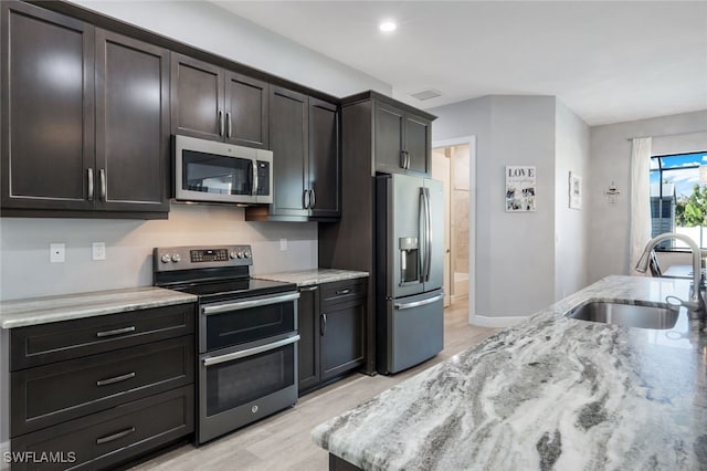 kitchen featuring dark brown cabinetry, sink, light wood-type flooring, appliances with stainless steel finishes, and light stone countertops