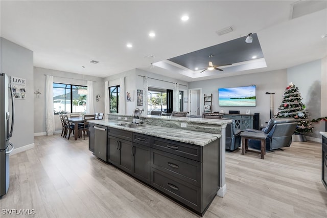 kitchen with sink, appliances with stainless steel finishes, light hardwood / wood-style floors, a center island with sink, and a raised ceiling