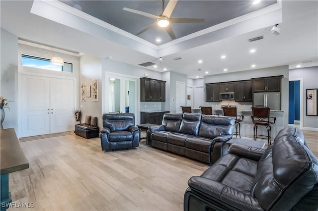 living room featuring ornamental molding, light hardwood / wood-style flooring, ceiling fan, and a tray ceiling