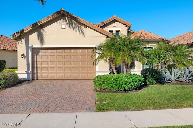 mediterranean / spanish home with a front yard, stucco siding, a garage, a tiled roof, and decorative driveway