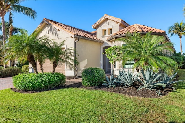 mediterranean / spanish-style house with stucco siding, an attached garage, a tile roof, and a front yard