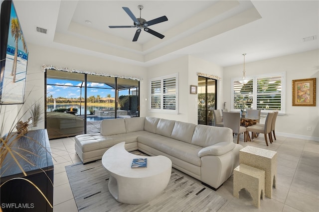 living room featuring light tile patterned floors, a water view, ceiling fan, and a tray ceiling