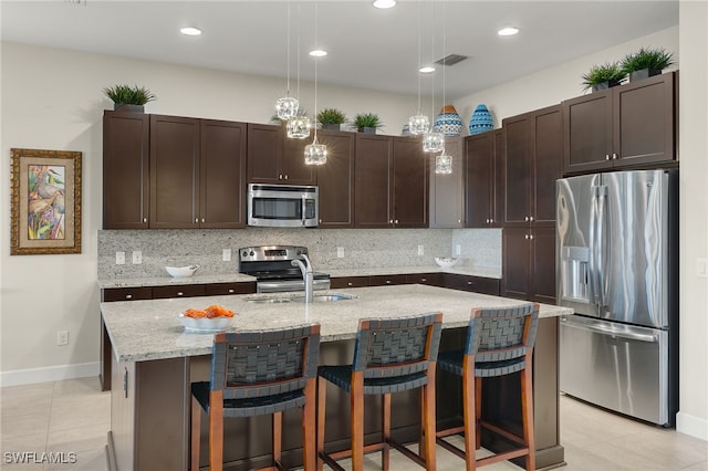 kitchen with pendant lighting, an island with sink, appliances with stainless steel finishes, tasteful backsplash, and dark brown cabinetry