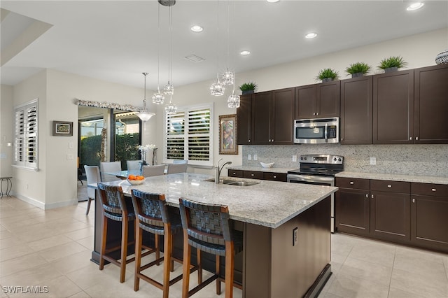 kitchen with decorative backsplash, stainless steel appliances, sink, pendant lighting, and an island with sink