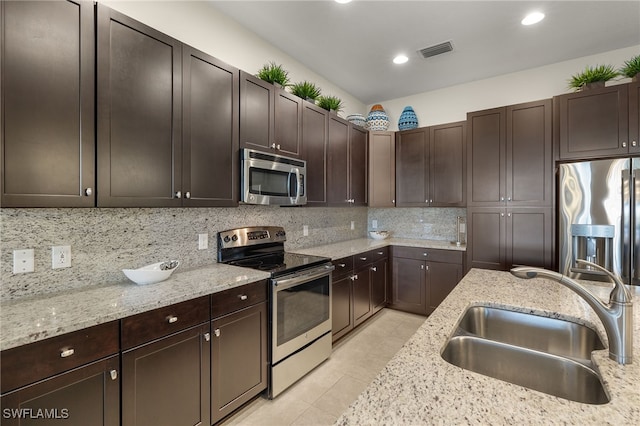 kitchen with dark brown cabinets, sink, light stone countertops, and stainless steel appliances