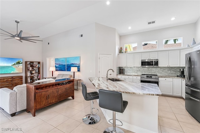 kitchen with white cabinetry, sink, stainless steel appliances, light stone counters, and a center island with sink