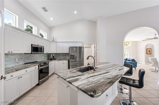 kitchen featuring a kitchen island with sink, sink, dark stone countertops, white cabinetry, and stainless steel appliances