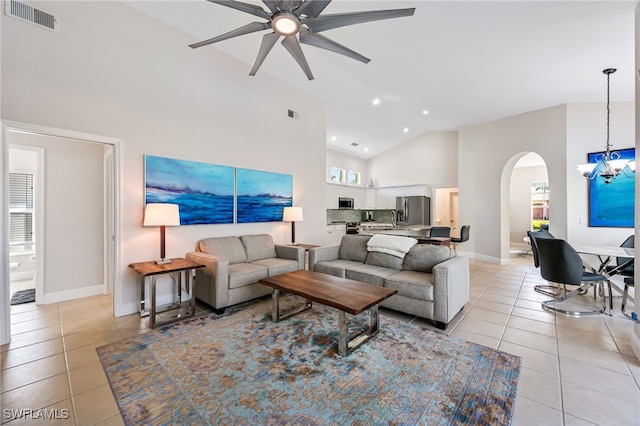 tiled living room with ceiling fan with notable chandelier and high vaulted ceiling