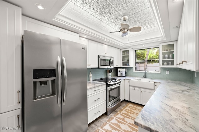 kitchen featuring light stone countertops, sink, a raised ceiling, white cabinets, and appliances with stainless steel finishes