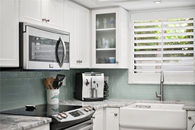 kitchen with backsplash, light stone counters, sink, electric stove, and white cabinetry