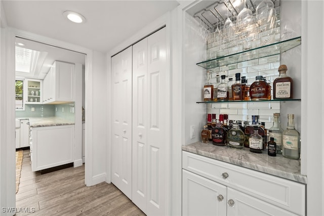 bar featuring white cabinetry, light hardwood / wood-style floors, and light stone counters