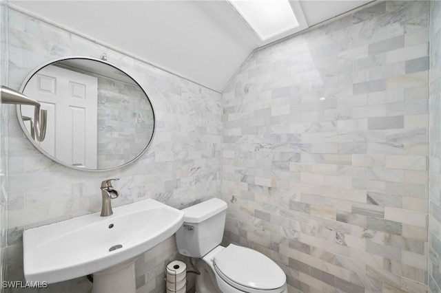 bathroom with toilet, sink, lofted ceiling, and tile walls