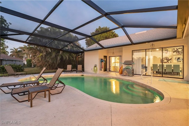 pool at dusk with glass enclosure and a patio