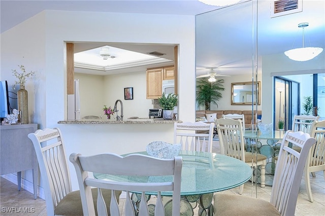 dining space with a toaster, visible vents, a tray ceiling, and a ceiling fan