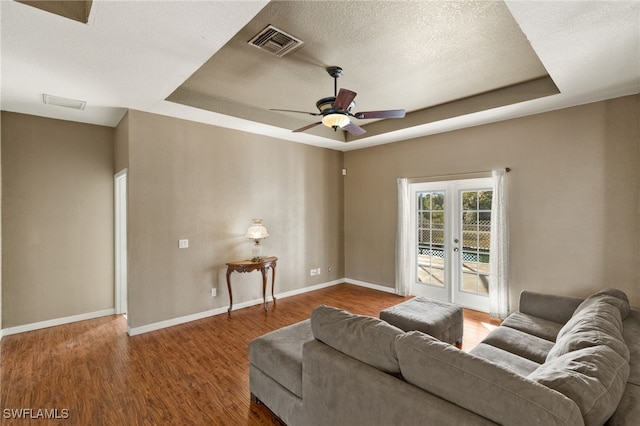 living room with ceiling fan, french doors, a raised ceiling, a textured ceiling, and hardwood / wood-style flooring