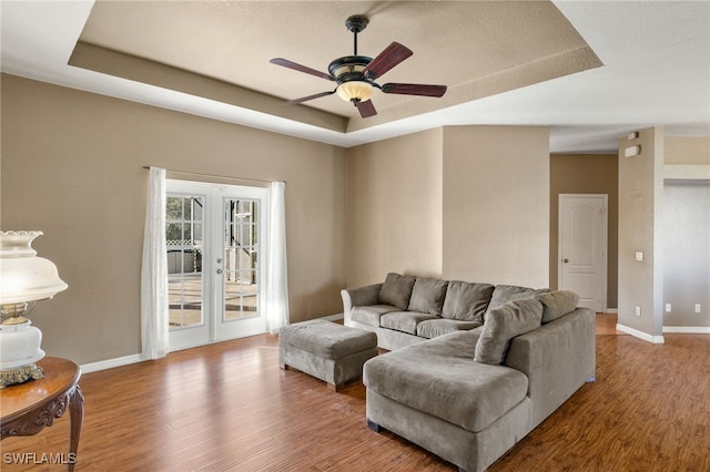 living room featuring a raised ceiling, ceiling fan, french doors, and hardwood / wood-style flooring