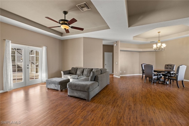 living room featuring french doors, ceiling fan with notable chandelier, a tray ceiling, and dark wood-type flooring