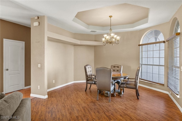 dining area featuring a raised ceiling, wood-type flooring, and a chandelier