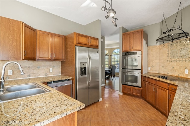 kitchen featuring decorative backsplash, appliances with stainless steel finishes, light stone countertops, sink, and decorative light fixtures