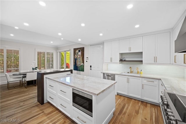 kitchen featuring sink, backsplash, appliances with stainless steel finishes, white cabinets, and light wood-type flooring