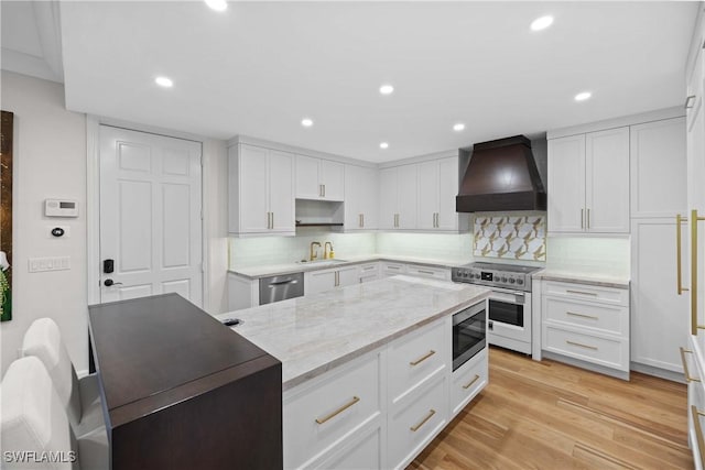 kitchen featuring sink, stainless steel appliances, premium range hood, white cabinets, and light wood-type flooring