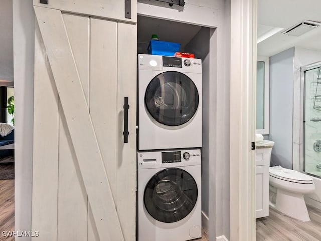 washroom featuring stacked washer / dryer, a barn door, and light hardwood / wood-style flooring