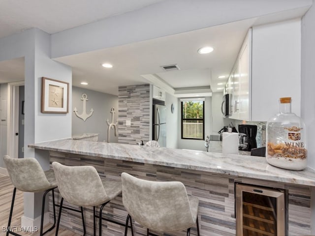 kitchen featuring wine cooler, appliances with stainless steel finishes, light stone countertops, and white cabinets