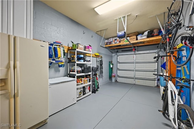 garage featuring white fridge with ice dispenser, concrete block wall, and refrigerator