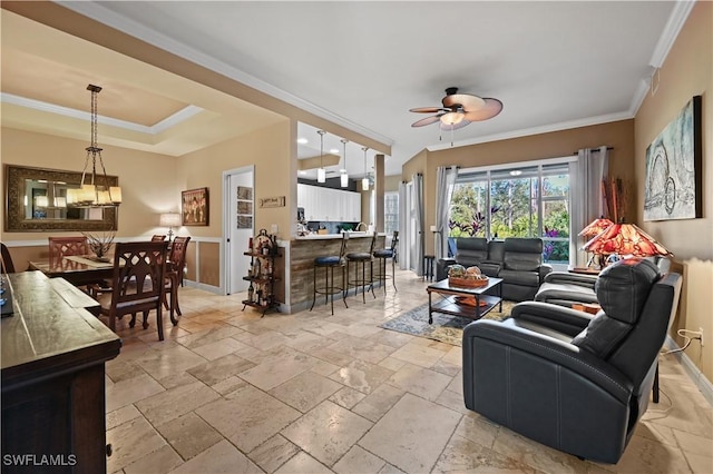 living room with a tray ceiling, stone tile flooring, a ceiling fan, and crown molding